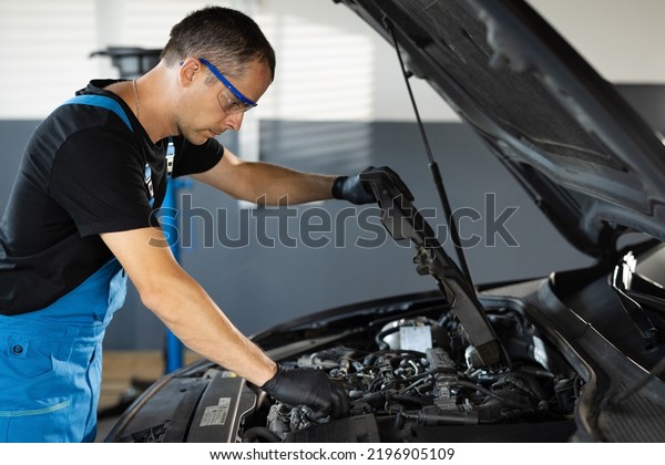 Mechanic man open a car hood and check up the\
engine. Car mechanic noting repair parts during open car hood\
engine repair at garage. Overheating of a car engine. Motor with\
open hood.