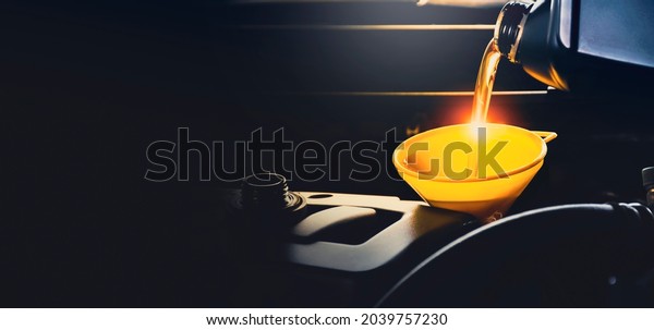 Mechanic man pouring lubricant oil to car\
engine in the repair garage with copy\
space