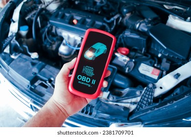 Mechanic man scanning ECU system of car engine by OBD2 wireless scanner tool with a car engine compartment background Car maintenance service concept