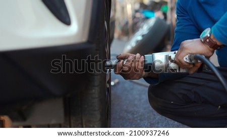 mechanic man using an electric drill to loosen the bolts of vehicle wheel for changing a car tire