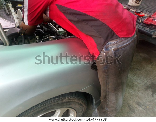 A mechanic, a man wearing a red shirt and\
wearing jeans, is repairing the\
car.