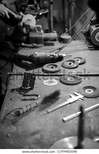 mechanic metal table, cuts the steel part with an\
angle grinder in the garage. In workshop, black and white\
technology in the workplace, eye protection. sparks fly in the eye,\
vertical photo