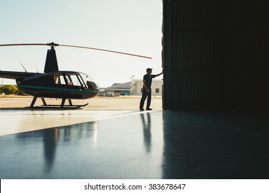 Mechanic Opening The Door Of A Airplane Hangar With A Helicopter