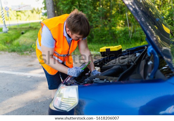 Mechanic in an orange vest with a diagnostic tablet\
checks the car engine. scheduled maintenance and diagnostics of the\
car engine. Mechanic With Digital Tablet Showing Graph While\
Examining Car