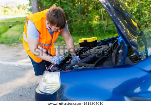Mechanic in an orange vest with a diagnostic tablet
checks the car engine. scheduled maintenance and diagnostics of the
car engine. Mechanic With Digital Tablet Showing Graph While
Examining Car