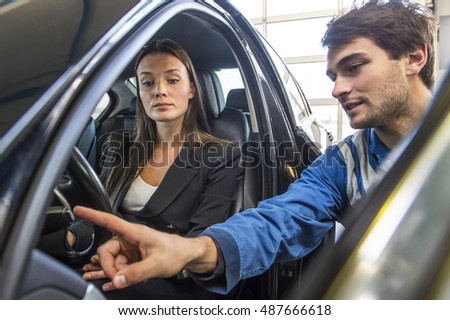 A mechanic in overalls explaining and instructing a customer, who has just bought a new car at a garage, as part of the after sales and service program