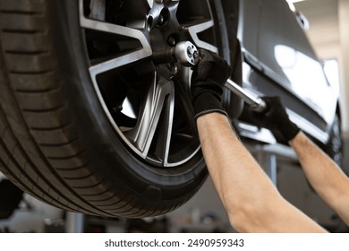 Mechanic performing tire maintenance using tools in auto repair shop. Close-up of gloved hands operating on car wheel, ensuring proper functionality and safety. - Powered by Shutterstock