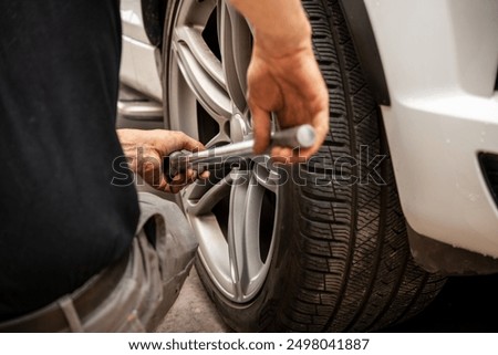 A mechanic performs tire maintenance using a wrench to tighten lug nuts on a vehicle's wheel, showcasing hands-on skills critical for automotive safety and efficiency.