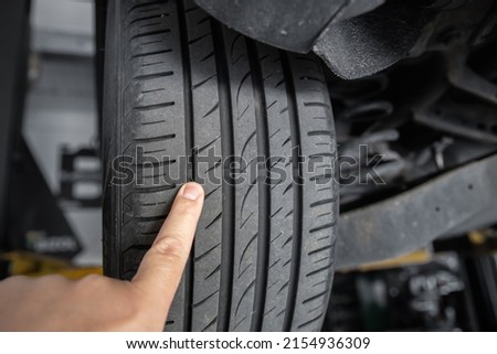 Mechanic pointing with hand at tyre wear indicator at car service center. Vehicle wheel protector control and inspection during maintenance. Tread wear check test inspection at automotive maintenance