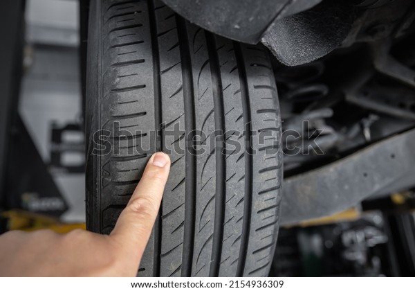 Mechanic pointing with hand at tyre wear\
indicator at car service center. Vehicle wheel protector control\
and inspection during maintenance. Tread wear check test inspection\
at automotive\
maintenance