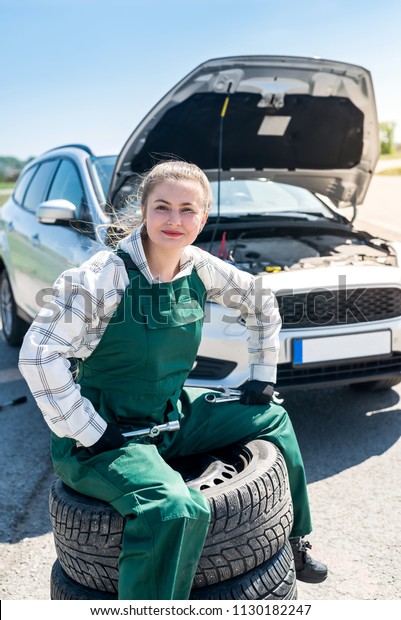 Mechanic posing\
with tyres on roadside with\
car