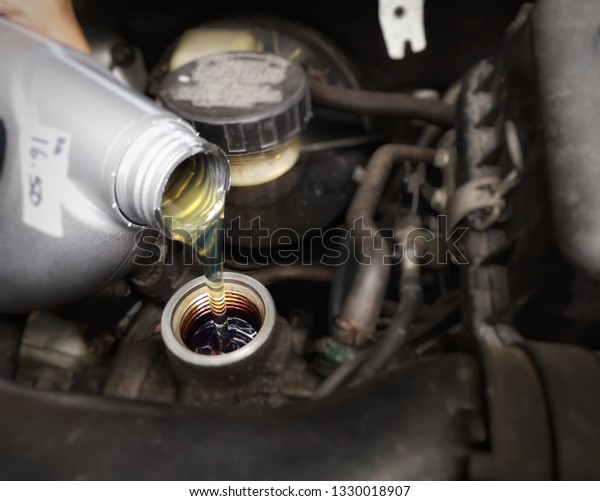 mechanic is pouring a motor car oil over an\
engine background