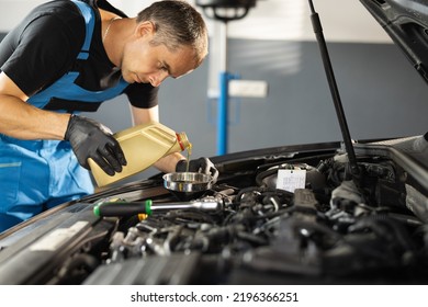 The mechanic is pouring oil into the engine. Pouring fresh oil to car engine, oil change to auto. Caucasian man in blue overalls pouring oil from plastic container. - Shutterstock ID 2196366251