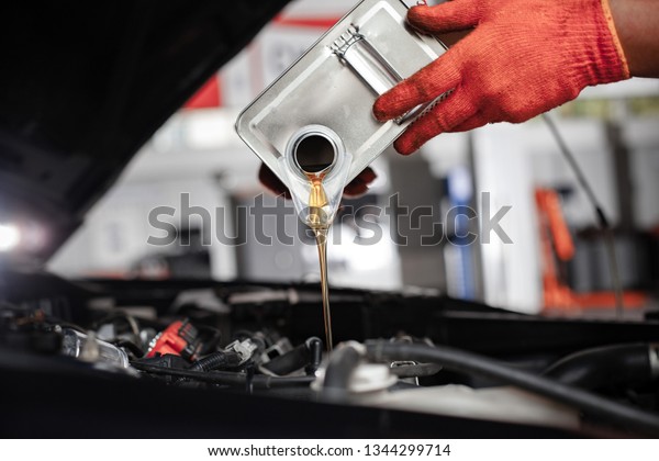 Mechanic is pouring oil into engine. Car hood is\
open. Change the oil.