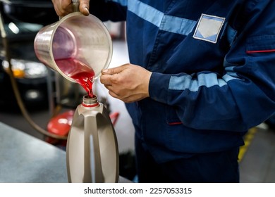 Mechanic pours oil into a canister. Changing the oil in a car engine in a service - Shutterstock ID 2257053315