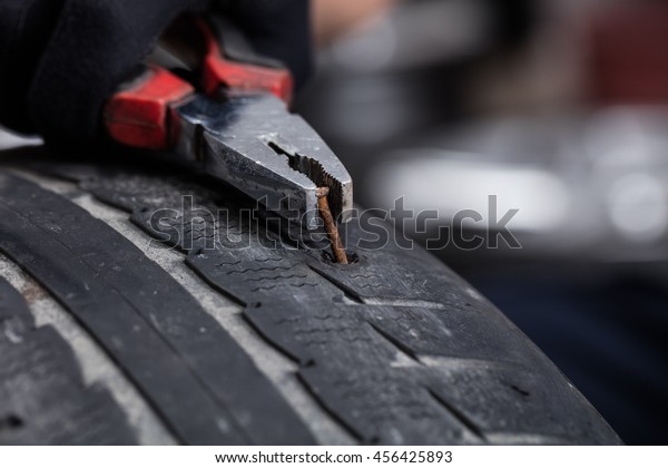 Mechanic pulling out metal screw\
nail need from car tire, picture of the tyre surface\
repair.