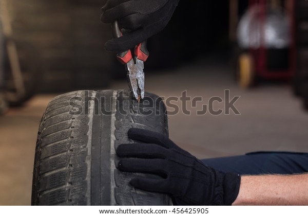 Mechanic pulling out metal screw\
nail need from car tire, picture of the tyre surface\
repair.