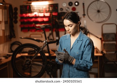 Mechanic reading a message on smartphone in bicycle workshop, she is repairing or servicing in a garage. Copy space - Powered by Shutterstock