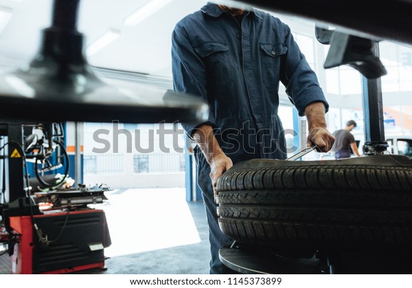Mechanic removes car\
tire service station. Man working on machine for removing rubber\
from the wheel disc.