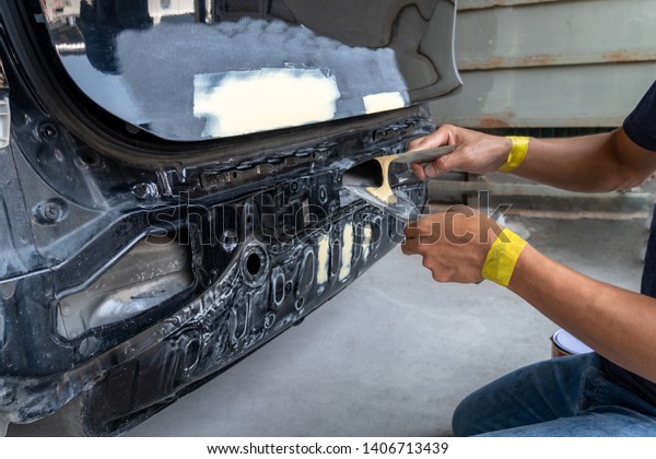 Mechanic repairing car\
body by puttying work after the accident by working sanding primer\
before painting.