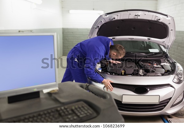 Mechanic\
repairing a car next to a computer in a\
garage