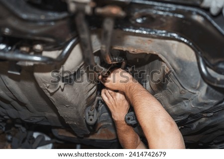 The mechanic is repairing the car from underneath, revealing the chassis and the transmission linkage.