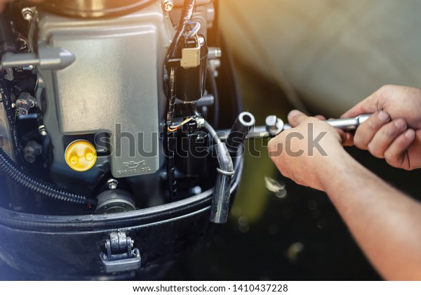 mechanic repairing inflatable motorboat engine at\
boat garage. Ship engine seasonal service and maintenance. Vessel\
motor with open cover
