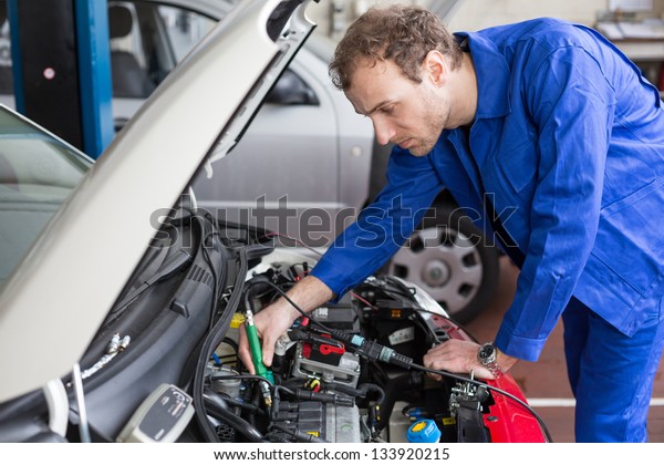 Mechanic repairing the motor or electric parts of\
a car in a garage
