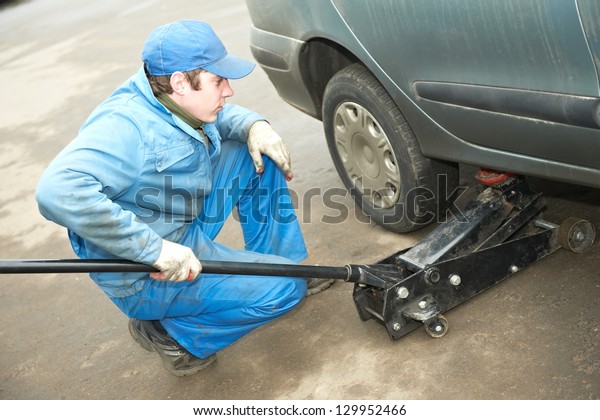 mechanic repairman making tyre fitting by using\
jack for car lifting