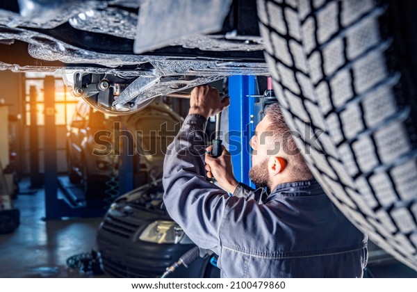 Mechanic repairs car chassis using a car\
lift. Auto service station\
background.