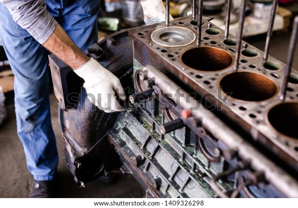 Mechanic repairs old motor of truck in a car
repair station. Disassemble engine block vehicle. Motor capital
repair. Car service
concept.