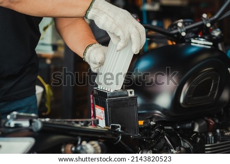mechanic replaces motorcycle battery and holding Acid pack or sealed battery electrolyte pack to prepare for fill up battery,motorcycle maintenance and service and repair concept . selective focus