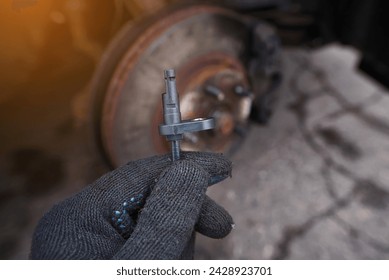 Mechanic replacing damaged ABS sensor. Man hold in hand new ABS sensor against car wheel background, ready to repair car. Abs sensor replacement - Automotive maintenance and repair service at work.