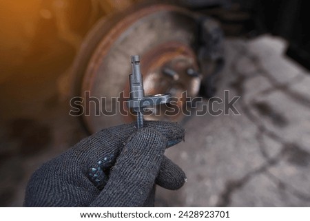 Mechanic replacing damaged ABS sensor. Man hold in hand new ABS sensor against car wheel background, ready to repair car. Abs sensor replacement - Automotive maintenance and repair service at work.