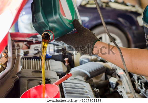 Mechanic replacing and pouring engine oil\
into engine car at maintenance service\
station