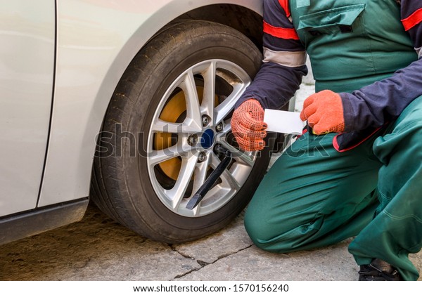 Mechanic in robe fixing car wheel. Car\
service concept with mechanic repairing\
car