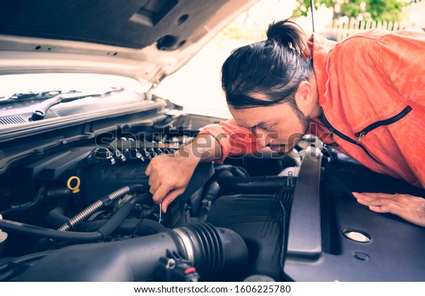 Mechanic with\
scan tool diagnosing car in open\
hood