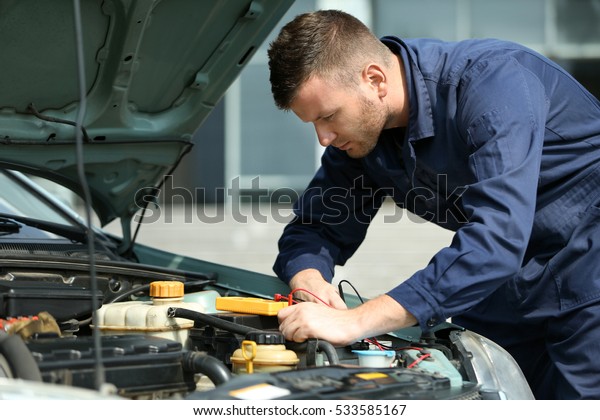 Mechanic with scan tool diagnosing car in open\
hood. Closeup