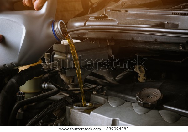 Mechanic in service to repair the\
car, refueling and pouring from bottle to change lubricant oil at\
maintenance repair service station, Energy fuel automotive\
concept
