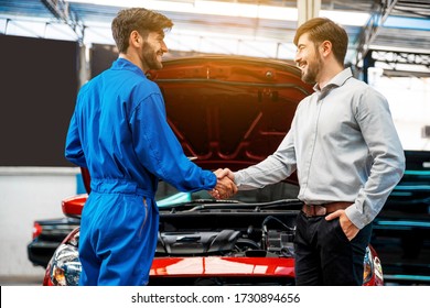 The mechanic shaking hands with customer after finish checking the opened hood red car. Focus on happy mechanic and satisfied customer. Auto car repair service center. Professional service. - Powered by Shutterstock