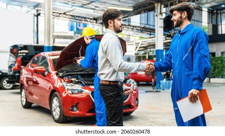 The mechanic shaking hands with customer after finish checking the opened hood red car. Focus on happy mechanic and satisfied customer. Auto car repair service center. Professional service. - Powered by Shutterstock