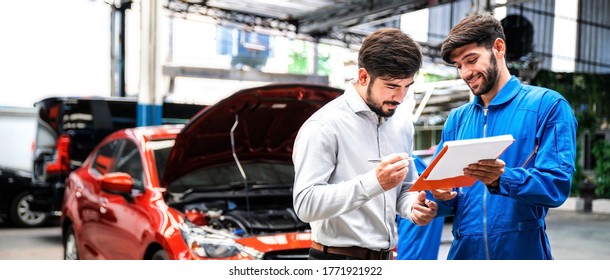 Mechanic show the car checking list for customer with blur his assistant checking red car. Focus on mechanic and customer on the right side. Auto car repair service center. Professional service.