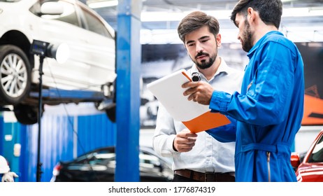 Mechanic show the car checking list to customer before giving him a car key with the blur lifted car in the garage. Focus on customer. Auto car repair service center. Professional service.