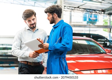 Mechanic show the car checking list to customer before giving him a car key with the blur lifted car in the garage. Focus on customer. Auto car repair service center. Professional service. - Shutterstock ID 2079450133