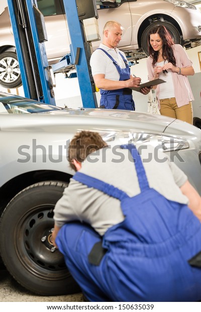 Mechanic\
showing  paperwork to car owner in\
garage