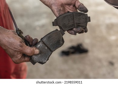 A Mechanic Showing Worn Disc Brake Pads Removed From A Car. Servicing And Replacing Old Parts Of A Vehicles At An Auto Repair Shop.