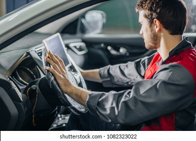 mechanic sitting in car doing diagnostics on digital tablet