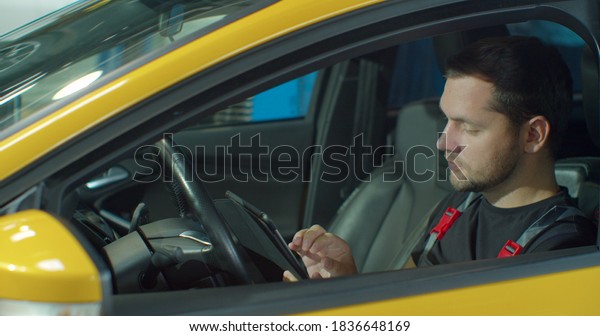 Mechanic sitting in car doing diagnostics on\
digital tablet.