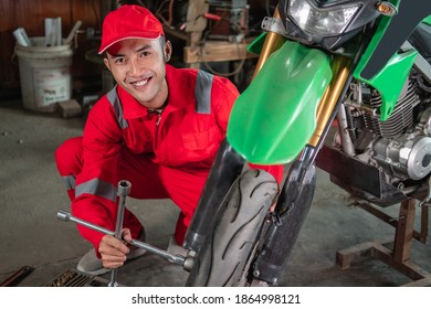 Mechanic Smiles At The Camera As He Uses The Wheel Nuts To Remove The Wheels Of The Motorbikes In The Repair Shop