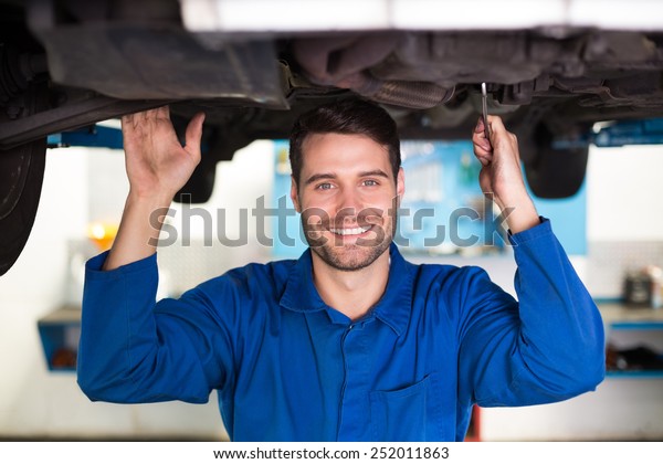 Mechanic smiling at the camera under car at the\
repair garage